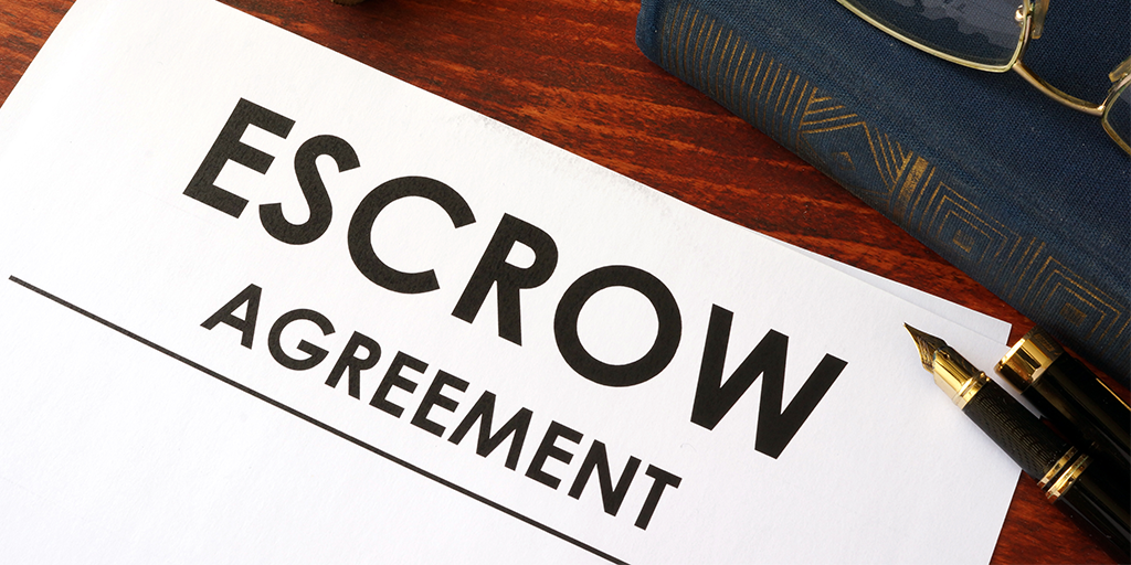 Paper with the words escrow agreement on a table with a pen and a book next to it