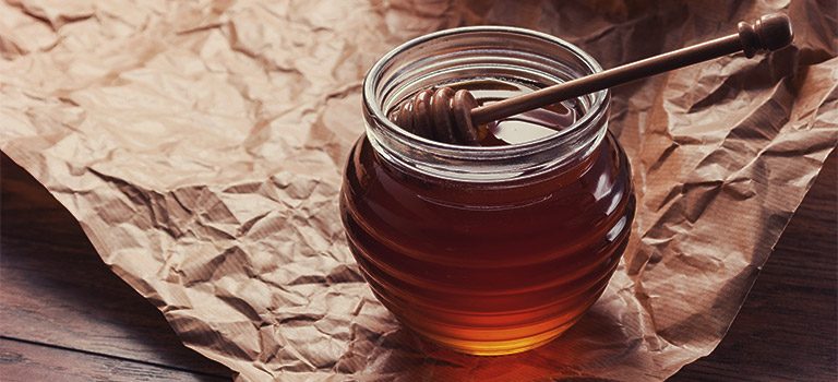 honeypot sitting on a brown paper on a table. Spoon in honey. Honey jar.