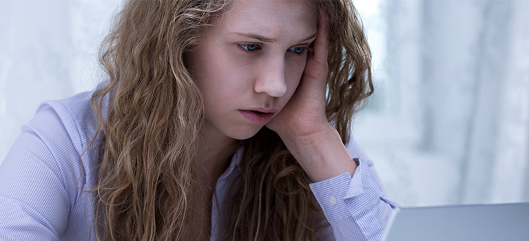 Girl looking upset while on computer, cyberbullying